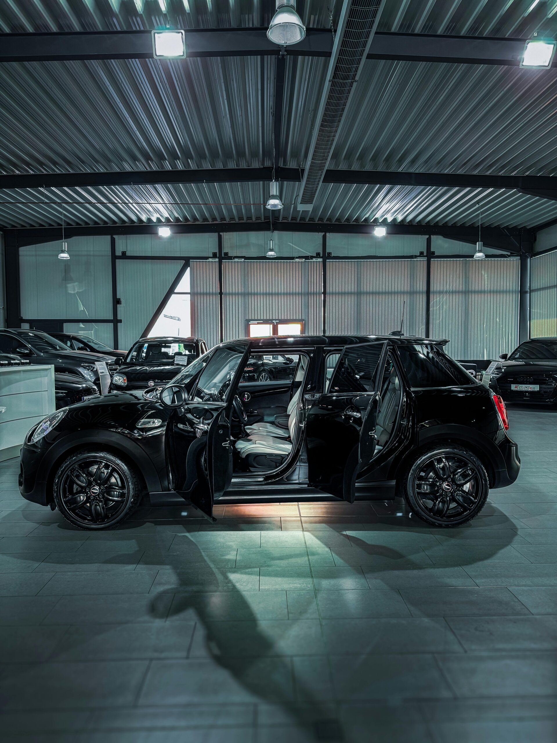 Side view of a black Mini Cooper with open doors in a spacious car showroom.